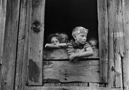 Children of miners look out the kitchen window of the Monroe Jones house.  The windows have no panes, the door frames have no doors; old quilts and boxes are used during the winter for protection.    Kentucky Straight Creek Coal Company, Belva Mine, 1946  Silver gelatin print  Russell Lee